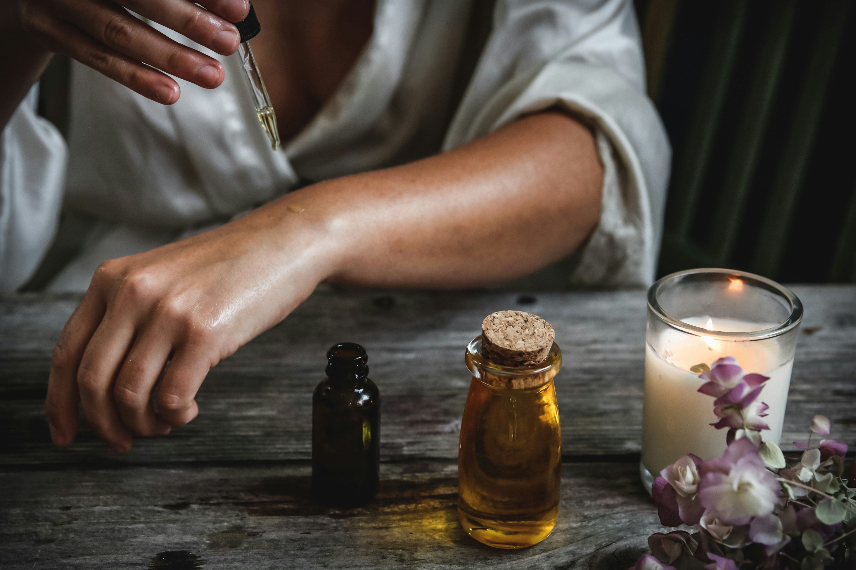 photo of a woman's arms and a a candle and essential oils 